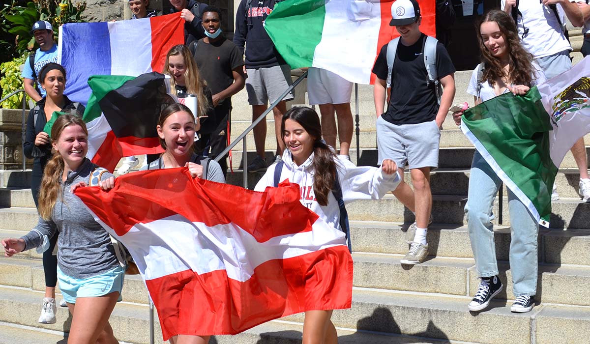 Students holding flags and laughing in front of the Modern Languages building
